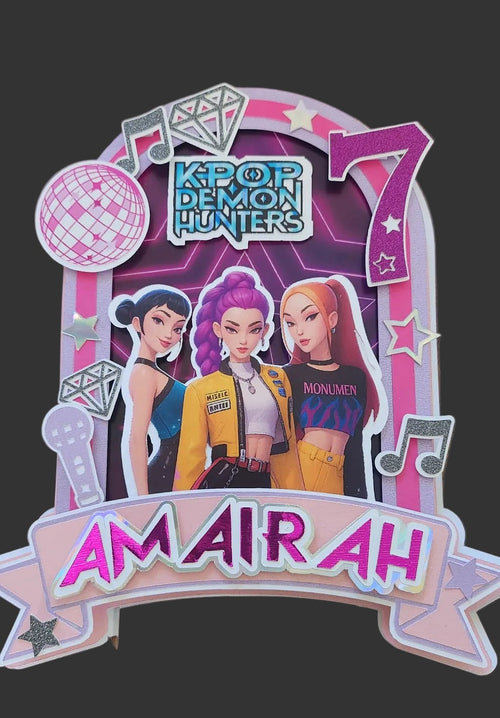 A decorative K-pop themed party decoration featuring characters from 'K-pop Demon Hunters' and the name on a pink and white banner